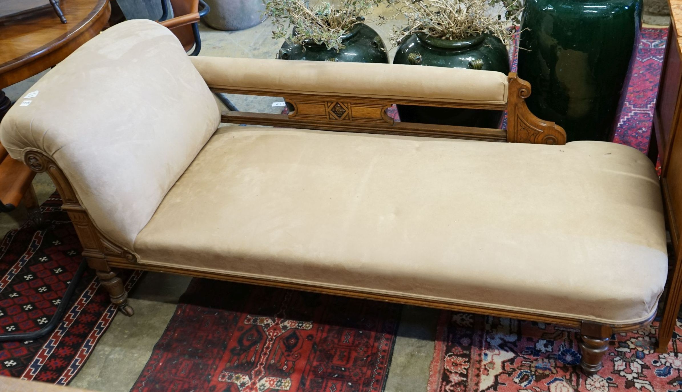 A late Victorian carved oak chaise longue upholstered in fawn suede, length 180cm, depth 70cm, height 79cm